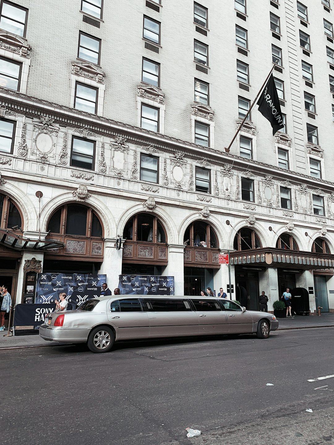 Srebrna limuzyna zaparkowana przed wejściem do okazałego kamiennego hotelu.